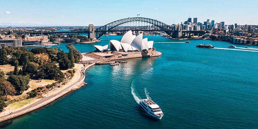 A cruise ship rides away from Sydney with the Sydney Opera House and Sydney Harbour Bridge behind it