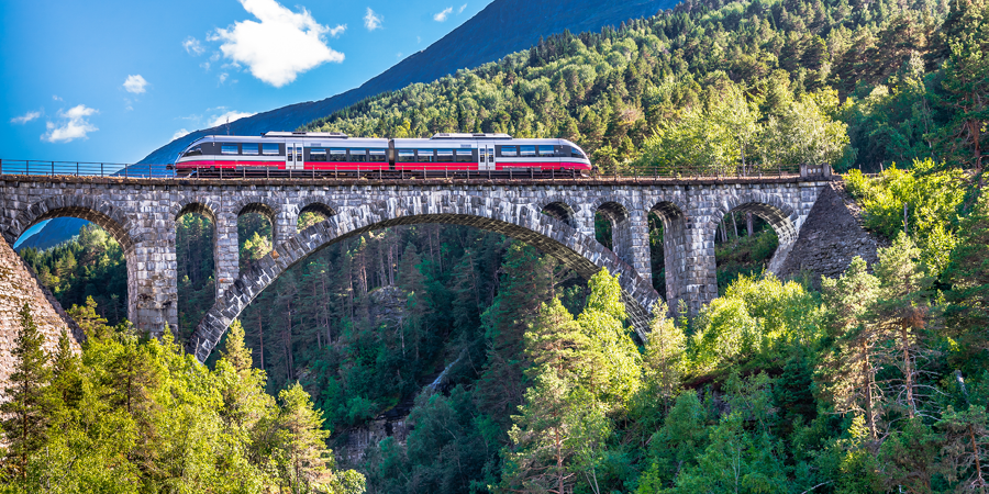 A silver train, with a stripe of red on its side, sat upon the Kylling bridge. 